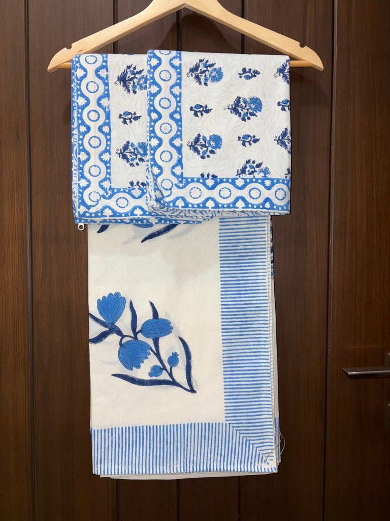 Set of blue and white patterned bedsheet hanging on a wooden hanger against a wooden door.