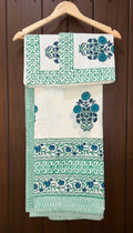 Set of green and white patterned bedsheet hanging on a wooden hanger against a wooden background.