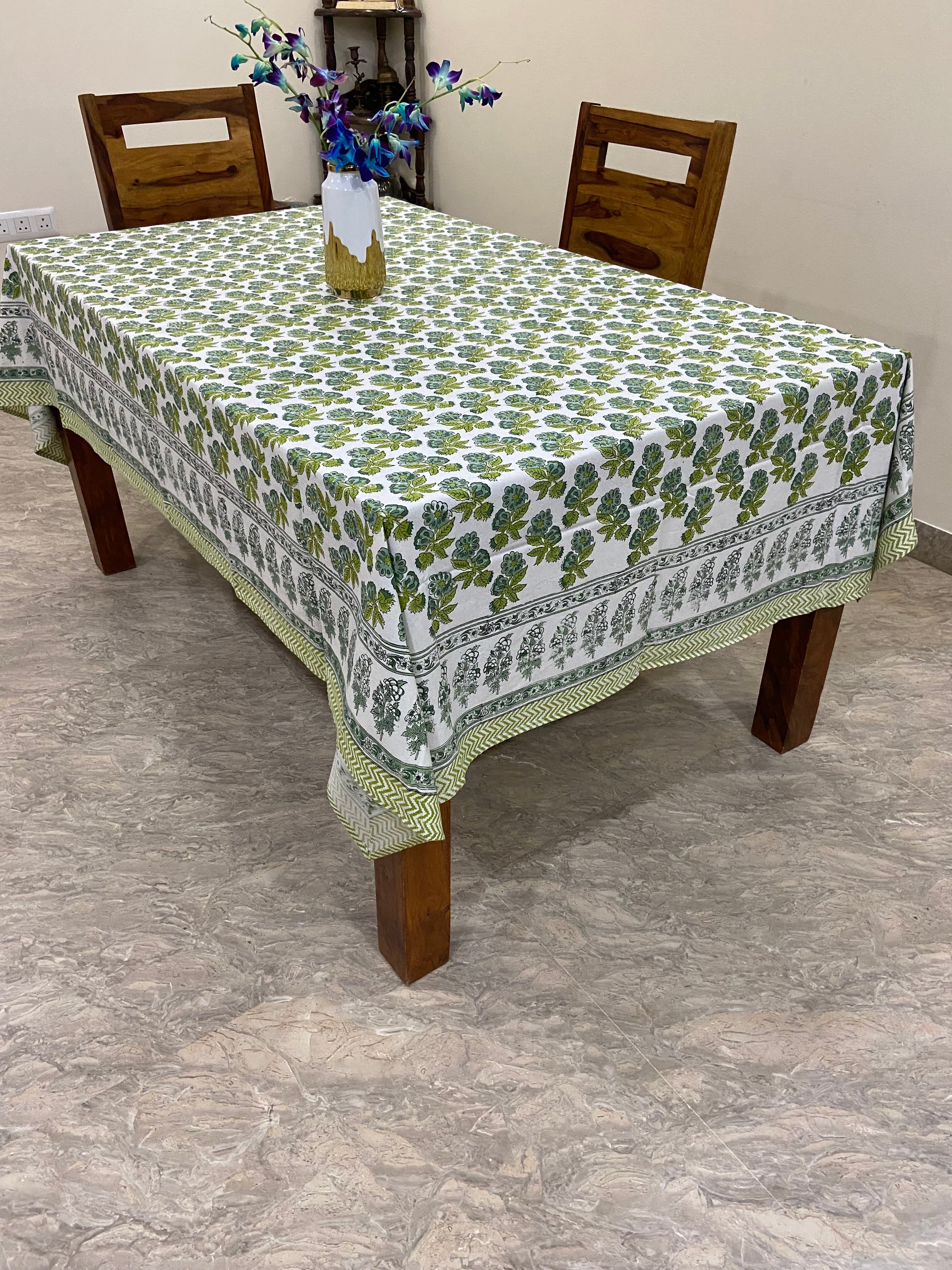 Table with a green and white patterned tablecloth on a marble floor.